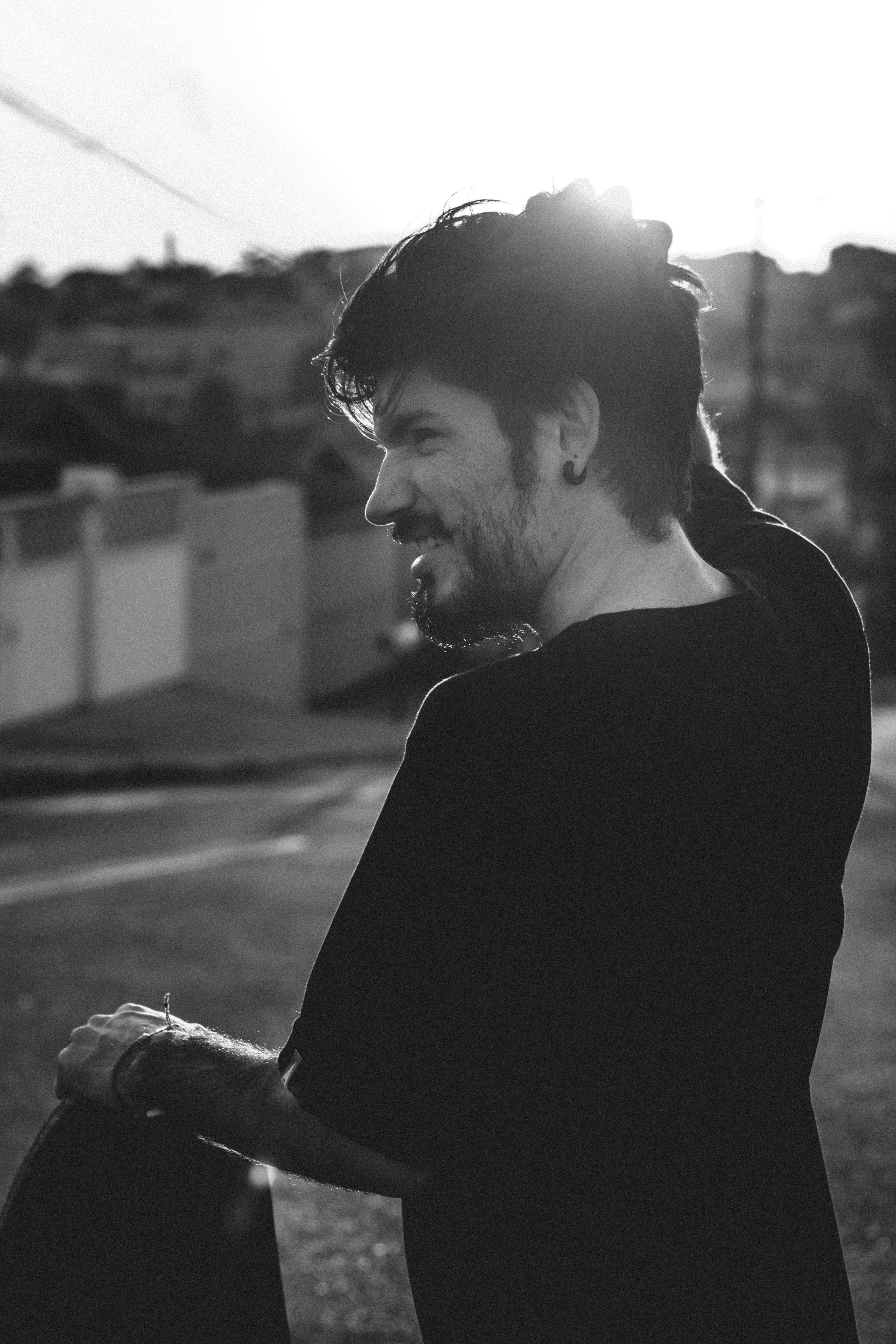 Black and white photo of a man outdoors, standing at sunset, capturing a thoughtful moment.