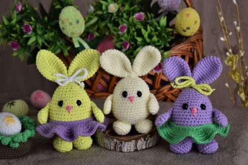 Free Vibrant trio of crocheted Easter bunnies with decorative eggs and flowers in a wicker basket background. Stock Photo
