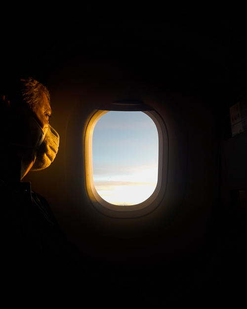 Free Silhouette of a masked passenger gazing at dawn sky through airplane window. Stock Photo