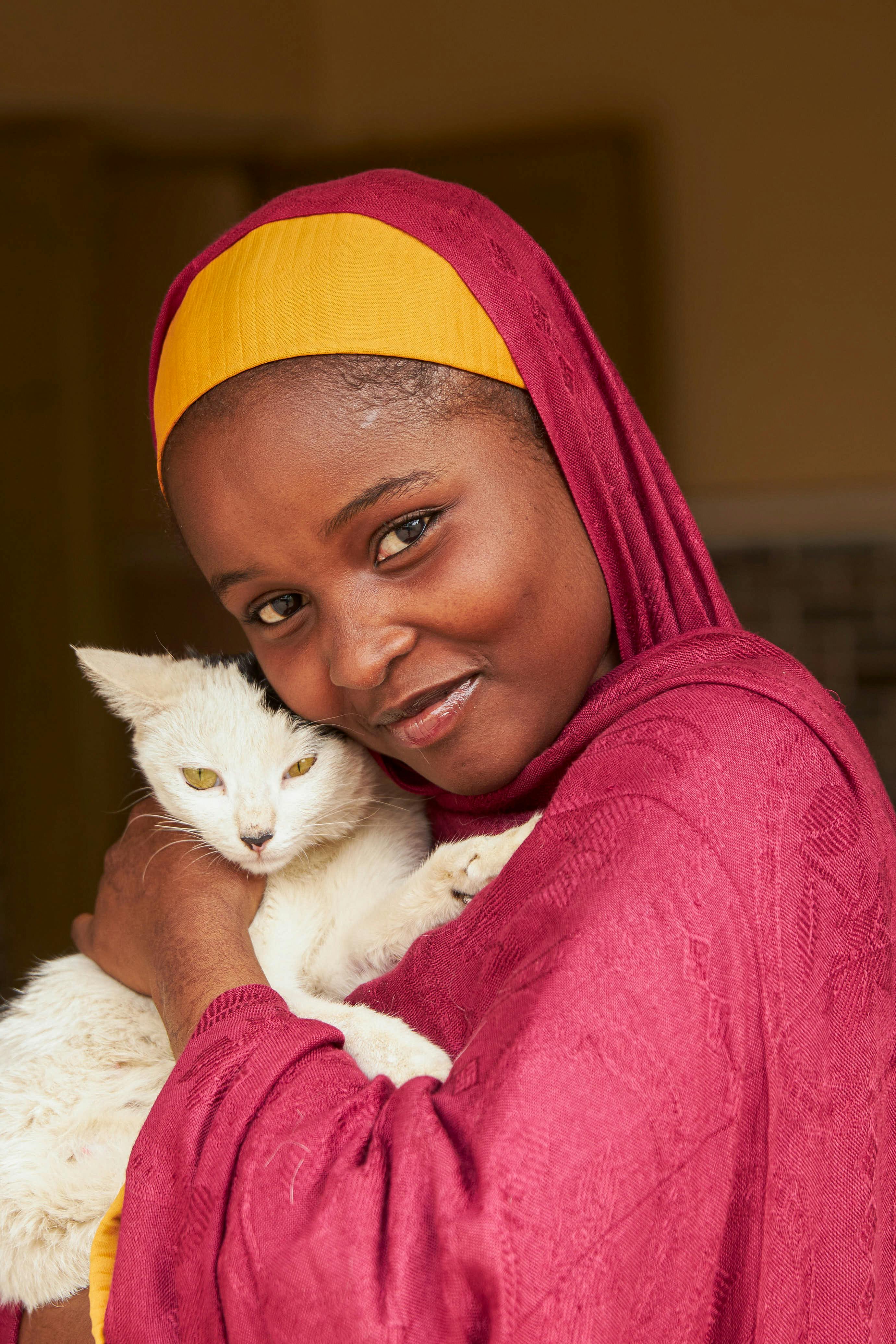 A joyful woman in a hijab holding a white cat, captured indoors.
