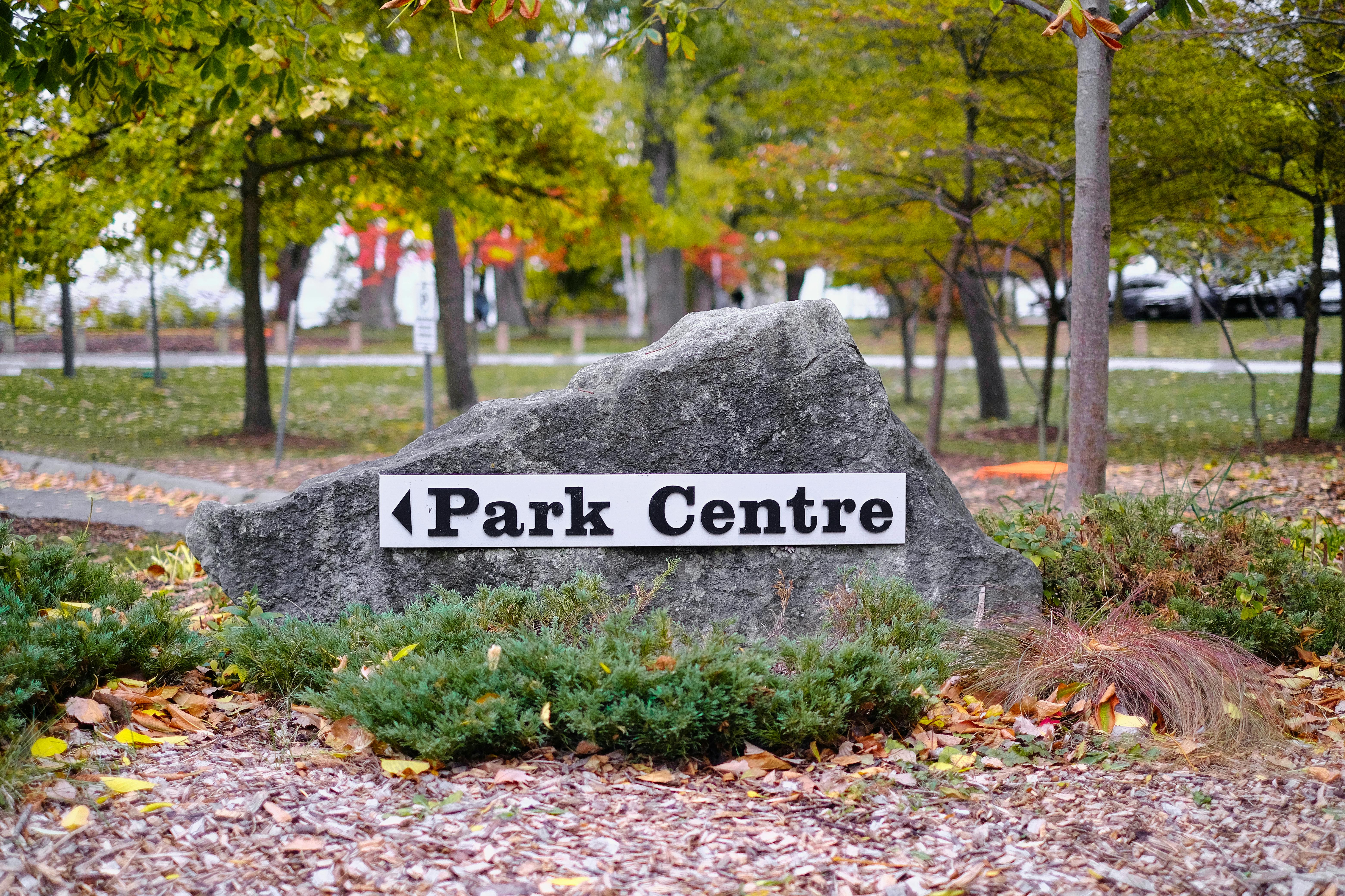 A stone sign with 'Park Centre' text in a park during the fall season.