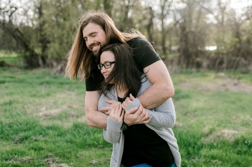 Free Happy couple embracing outdoors, enjoying a sunny day in a wooded park area. Stock Photo