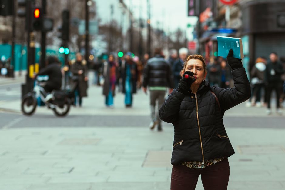 Woman preaching on the street with a microphone, holding a book in a busy urban area.