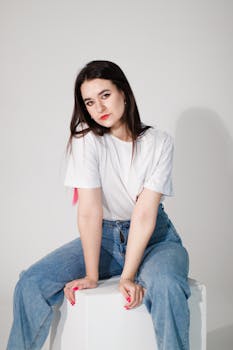 A young woman sitting confidently in casual attire against a plain background.