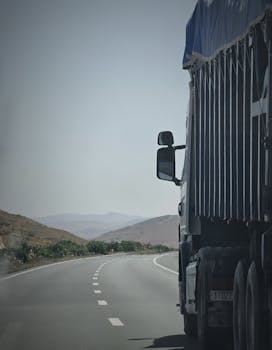 Truck on a winding highway in Douar Ouled El Mesnaoui, Morocco, set in a rocky landscape.