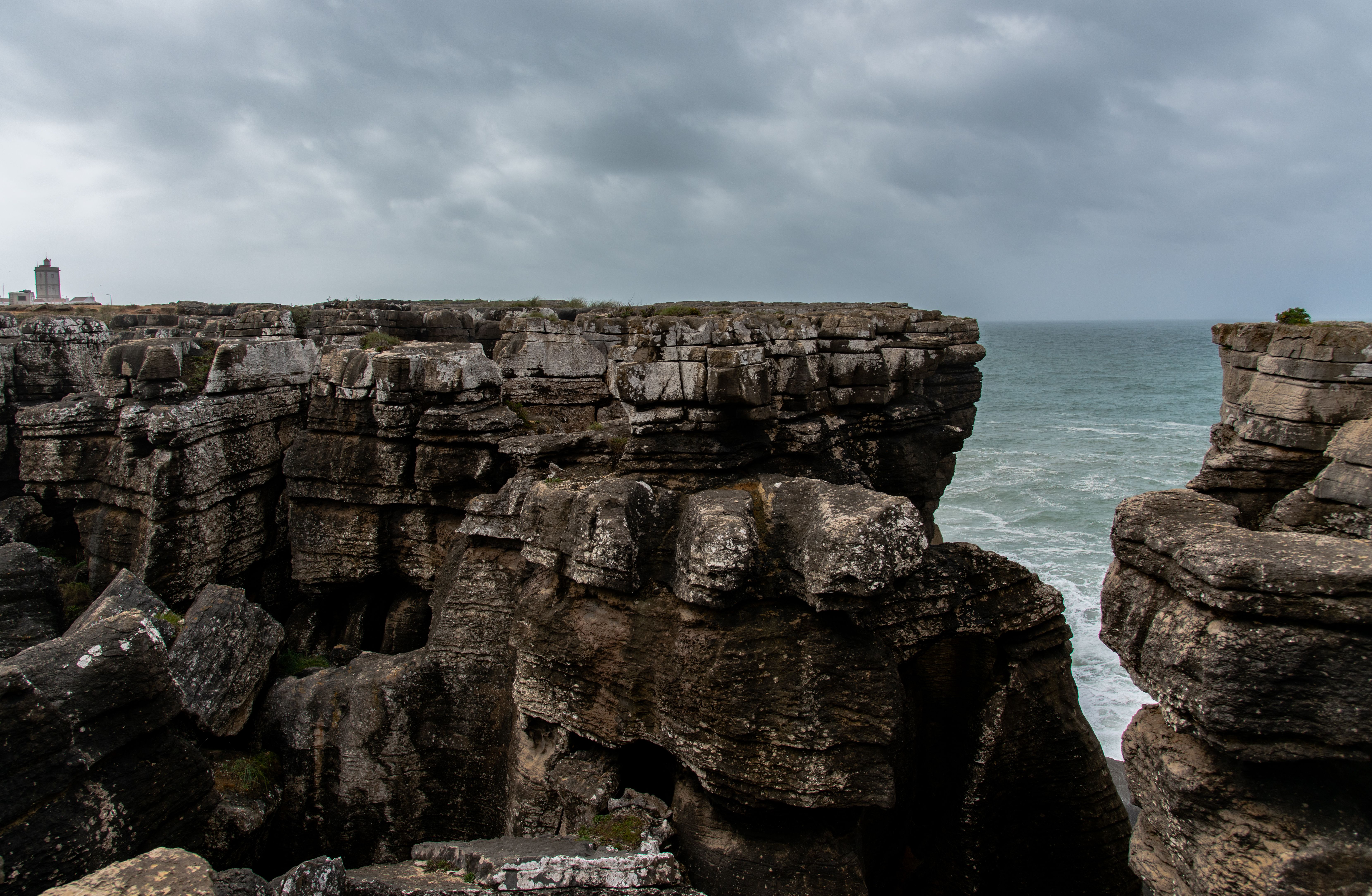 Scenic view of rugged cliffs meeting the Atlantic Ocean under a cloudy sky, Peniche, Portugal.