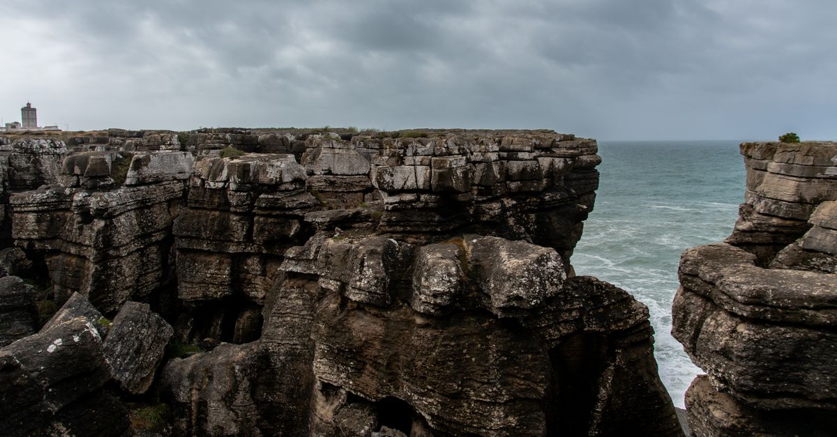 Scenic view of rugged cliffs meeting the Atlantic Ocean under a cloudy sky, Peniche, Portugal.