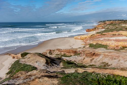 Free Breathtaking view of a sandy beach with rocky cliffs and rolling waves on a sunny day. Stock Photo
