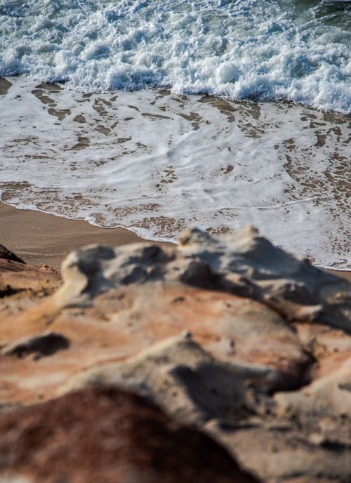 Free Beautiful coastal scene with waves crashing on sandy shore against rocky foreground. Stock Photo