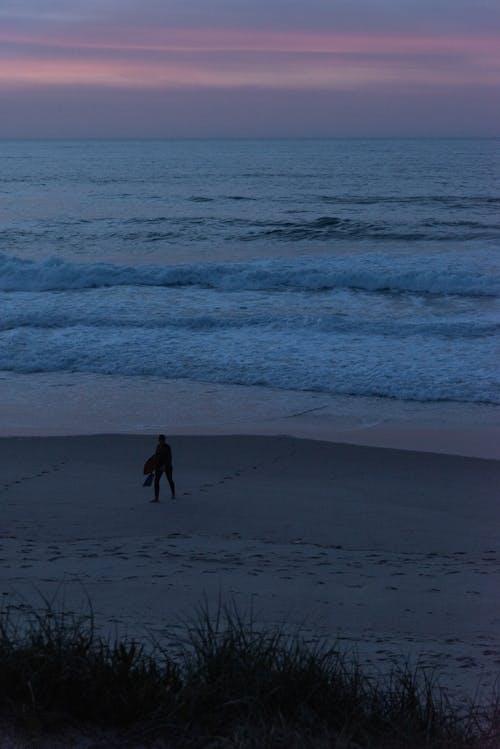 Aerial View of a Person Walking Alone on a Beach at Sunset