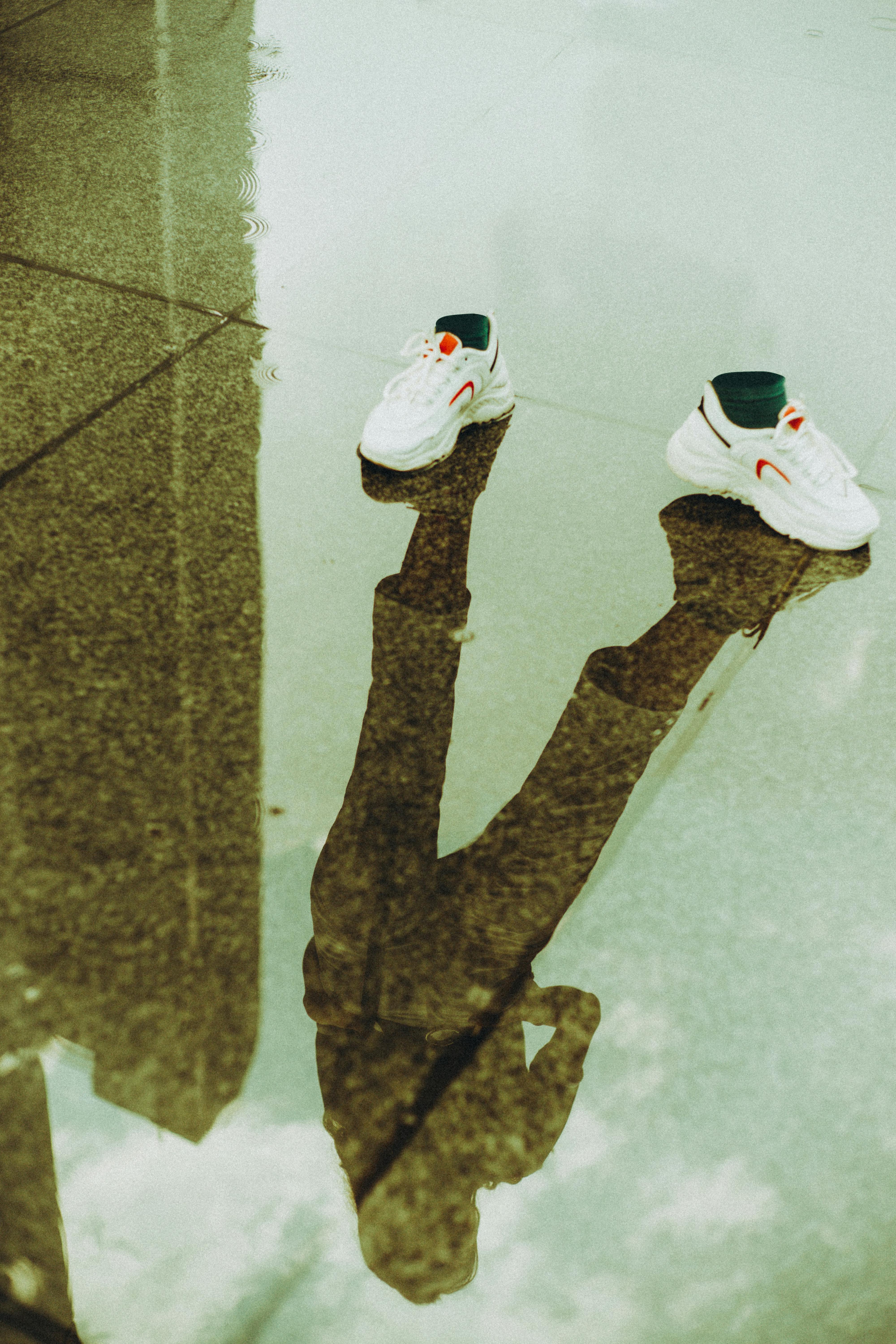 White sneakers with a reflection in a rain puddle on an urban street, creative high angle capture.