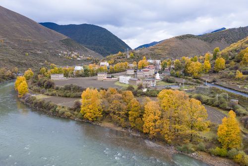 Free Aerial view of a quaint village surrounded by autumn trees with a river flowing nearby. Stock Photo