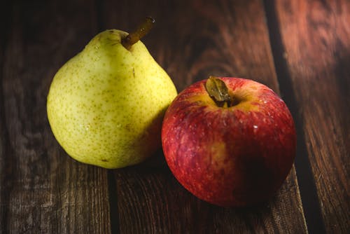 Close-up of a Red Apple and Green Pear Lying on a Wooden Surface