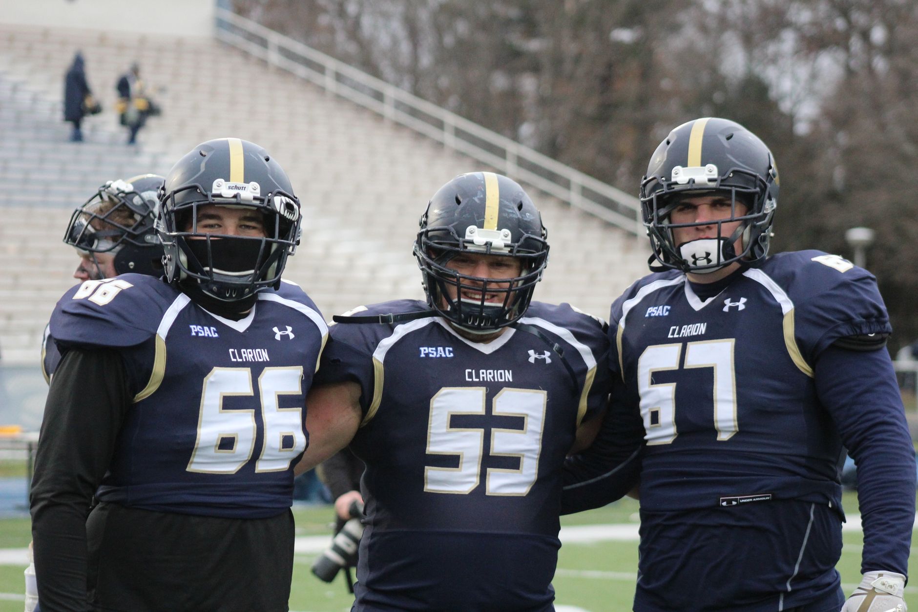 Three football players pose in uniforms at a college stadium, showcasing teamwork and sportsmanship.
