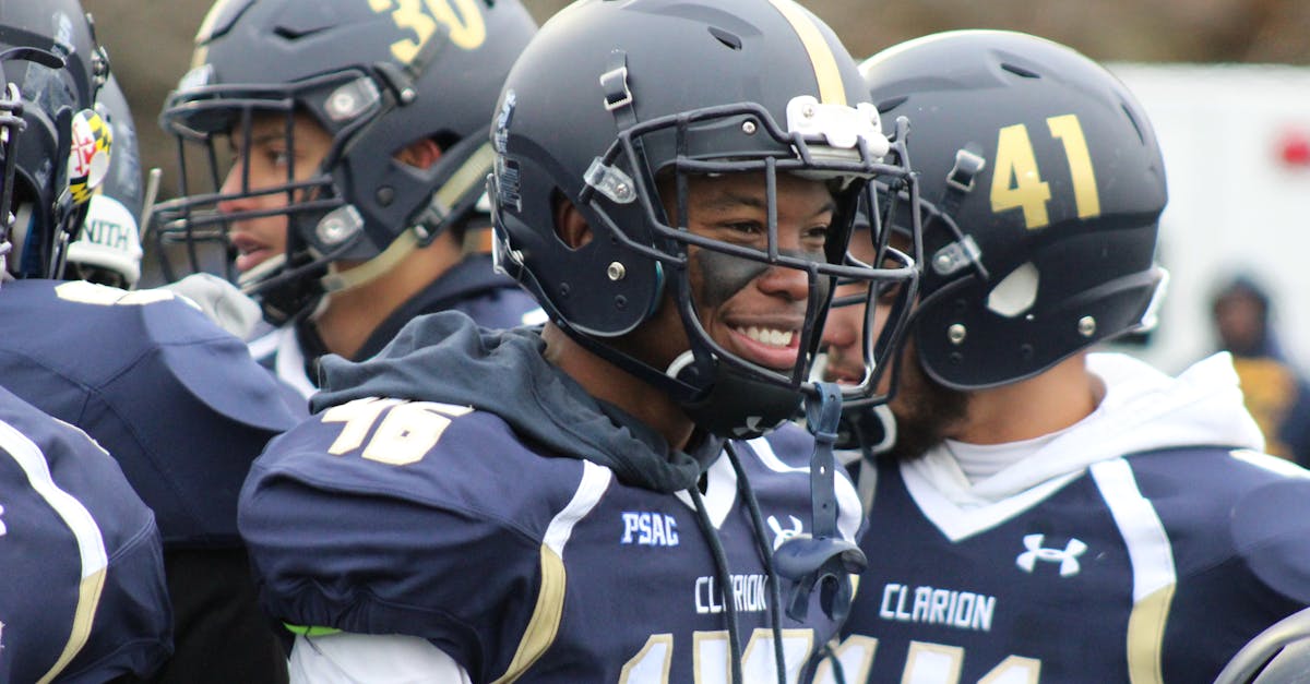 American football players in helmets and uniforms smiling on sidelines during a game