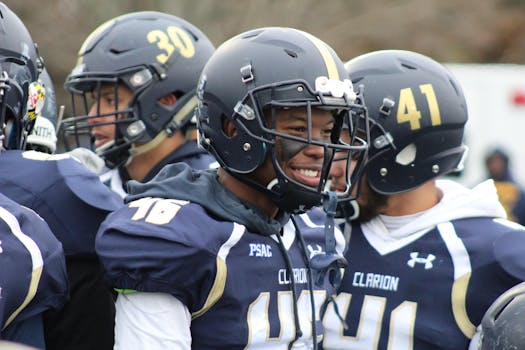 American football players in helmets and uniforms smiling on sidelines during a game