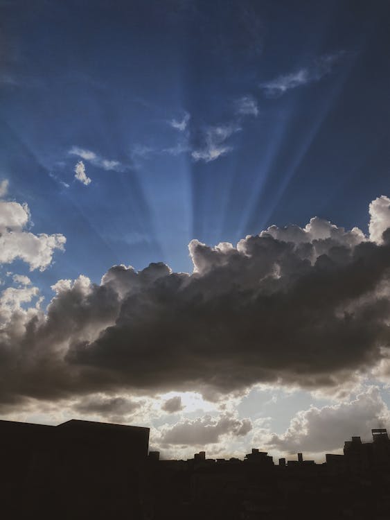 Sunlight behind Clouds over Buildings Silhouette at Sunset