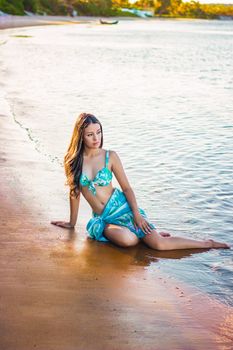 A young woman in a turquoise swimsuit relaxing on a sandy beach in Brazil.