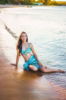 Beautiful young woman posing in a turquoise bikini on a serene beach.