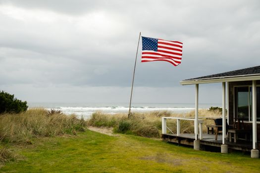 A coastal scene featuring an American flag waving near a seaside hut with an overcast sky.