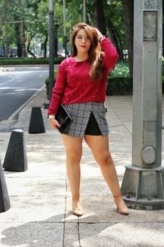 Woman in red blouse posing stylishly on a city sidewalk.