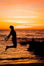 日落时分，一名男子在海滩上快乐跳跃的剪影映衬着壮丽的海洋