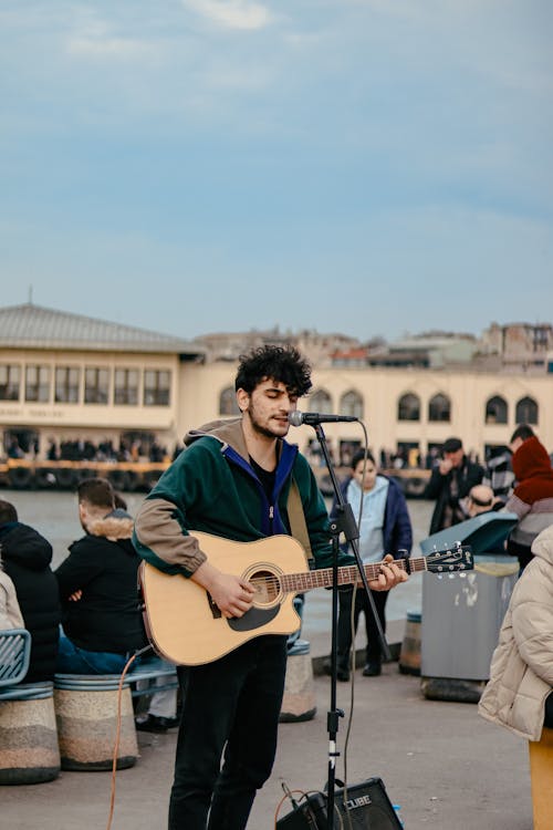 Young Man Playing Acoustic Guitar and Singing on a Town Square