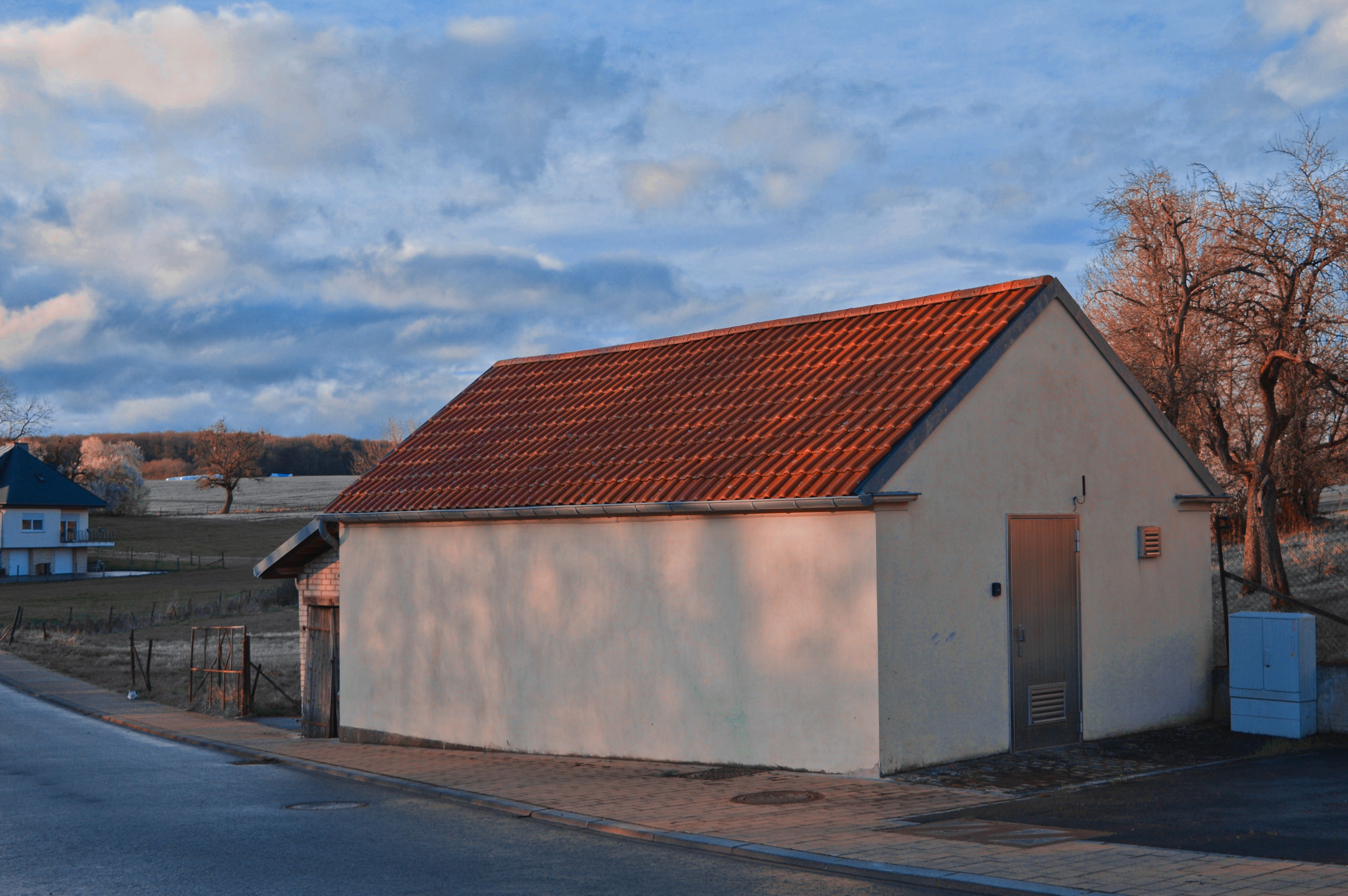 Rural building with a red tile roof under a cloudy sky.