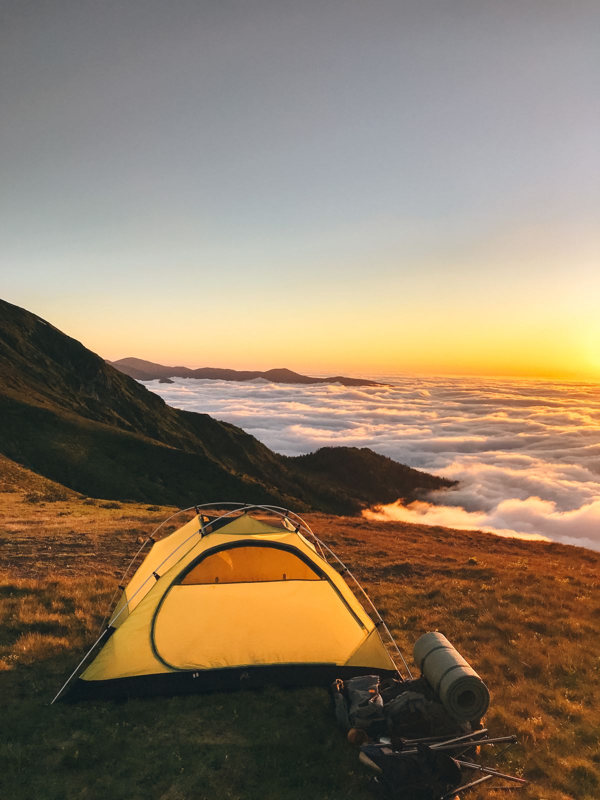 Yellow tent on a hilltop above the clouds at sunrise