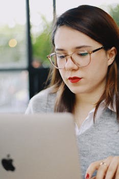 A woman with eyeglasses and red lips working on a laptop in a cafe setting.