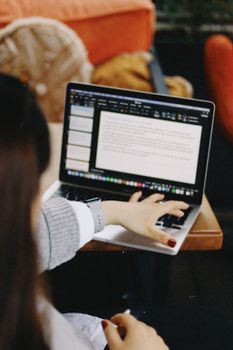 Young woman working on a laptop in a cosy café setting, focusing on typing and productivity.