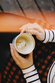 A close-up top view of a woman holding a coffee cup with latte art, wearing a striped sweater.. close, view, woman