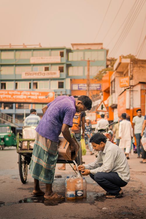 Free Two men filling plastic bottles from a cart in a busy urban marketplace street. Stock Photo
