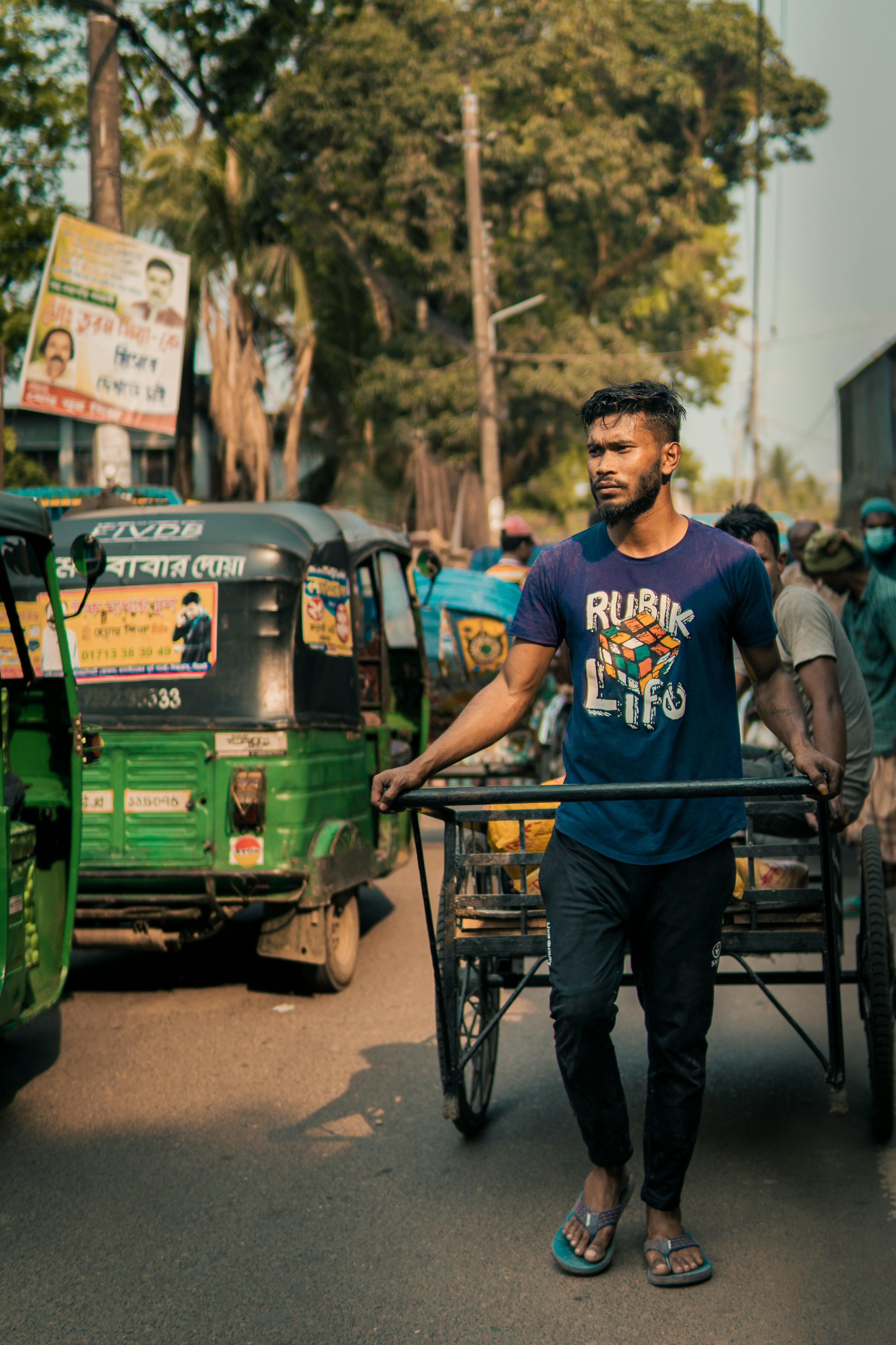 A man pulls a cart through a busy urban market street, surrounded by vehicles and street vendors.