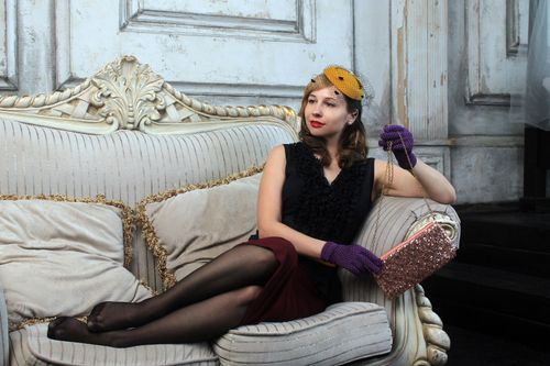 Free A stylish woman in vintage attire, sitting elegantly on a sofa with a clutch bag. Stock Photo