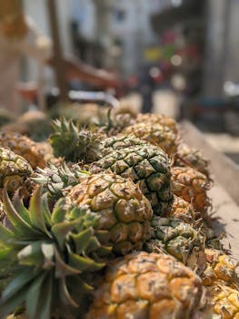 Fresh pineapples in an urban market setting, captured in a close-up view with sunlit effects.