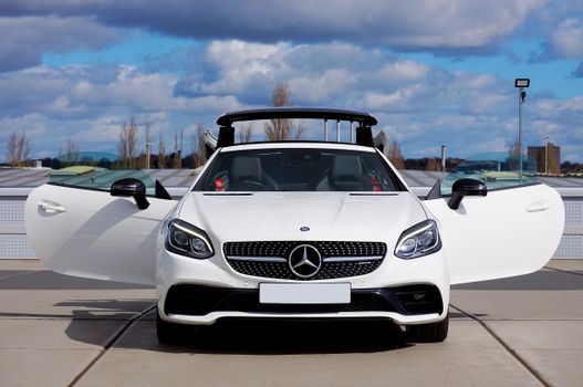 A sleek white convertible car with open doors parked outdoors under a vibrant sky.
