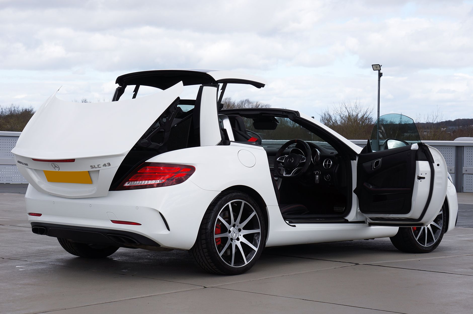 Elegant white Mercedes-Benz SLC convertible with open doors and roof parked outdoors.