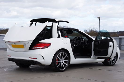Elegant white Mercedes-Benz SLC convertible with open doors and roof parked outdoors.