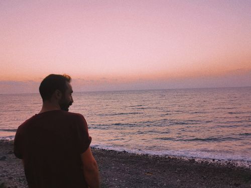 Free A man gazes out over the ocean during a tranquil sunset with a pink sky. Stock Photo