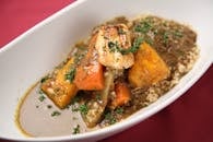 粉红色背景上，特写着一锅丰盛的炖菜，以烤肉、蔬菜和蒸粗麦粉为特色