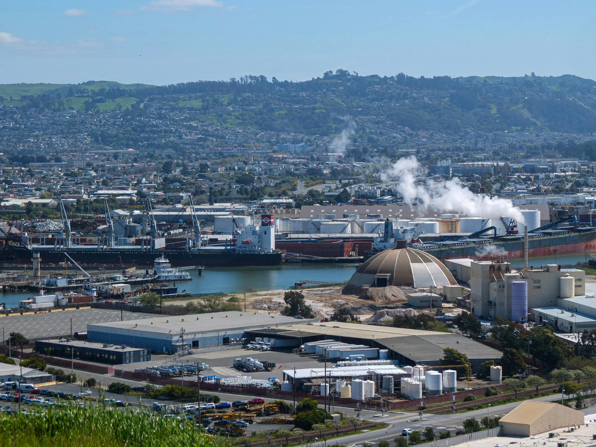 Cargo ships and industrial buildings seen from above in a bustling harbor.