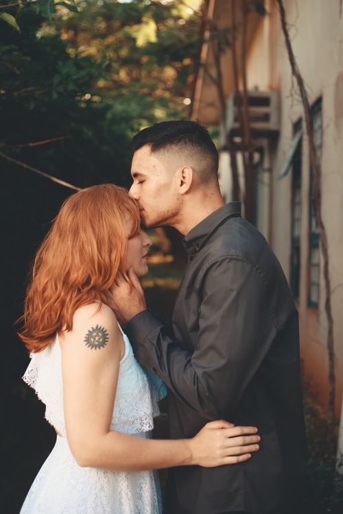 Free A couple sharing a tender forehead kiss, expressing love and affection outdoors. Stock Photo