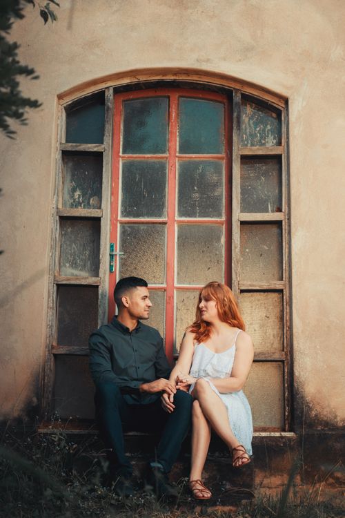 Free A young couple sitting and holding hands on rustic steps, surrounded by a classic facade. Stock Photo