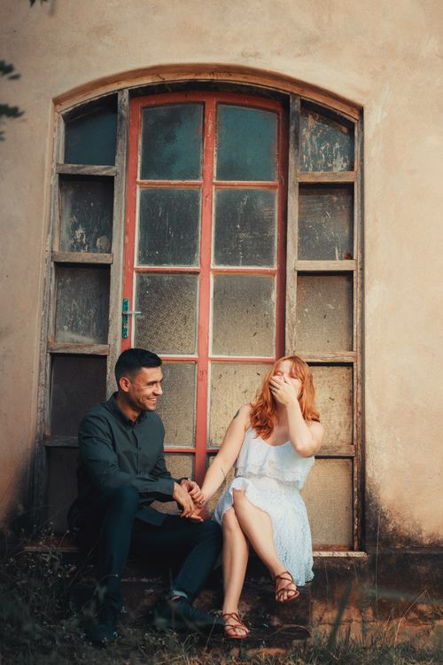 Free Laughing couple sitting by a rustic doorway, capturing a moment of joy. Stock Photo