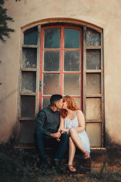 Free A loving couple shares a romantic kiss sitting in front of a vintage door. Stock Photo