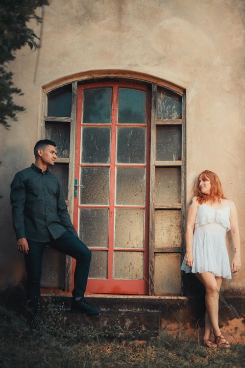 Free A young couple poses stylishly by a rustic red door outdoors. Stock Photo