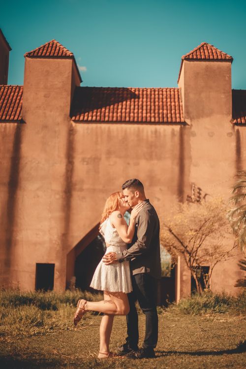 Free A couple shares a romantic moment outdoors near a rustic brick building on a sunny day. Stock Photo