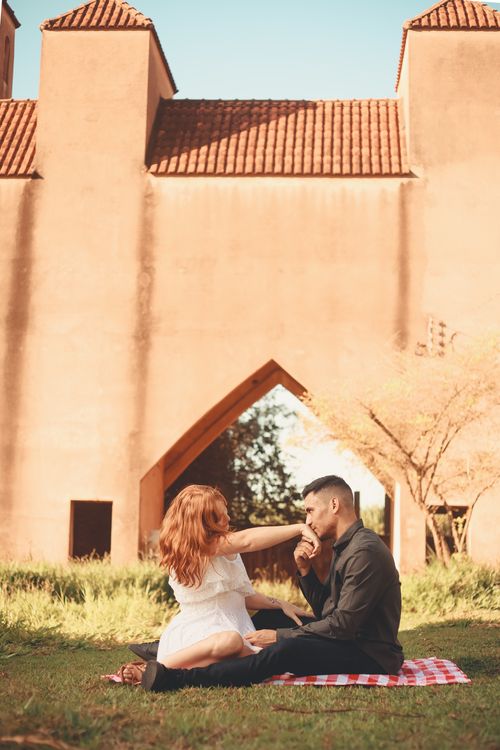 Free A couple sharing a romantic moment during a sunlit picnic by a rustic building. Stock Photo