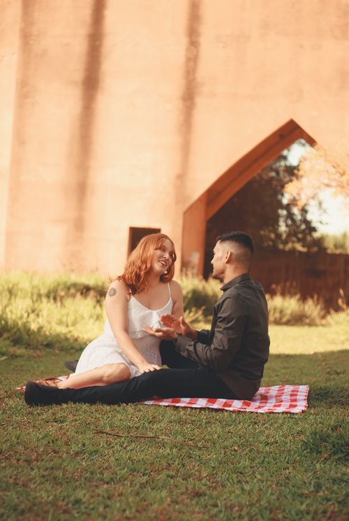 Free A couple enjoys a romantic picnic on a sunny day by a historic wall, sharing smiles and a moment of connection. Stock Photo